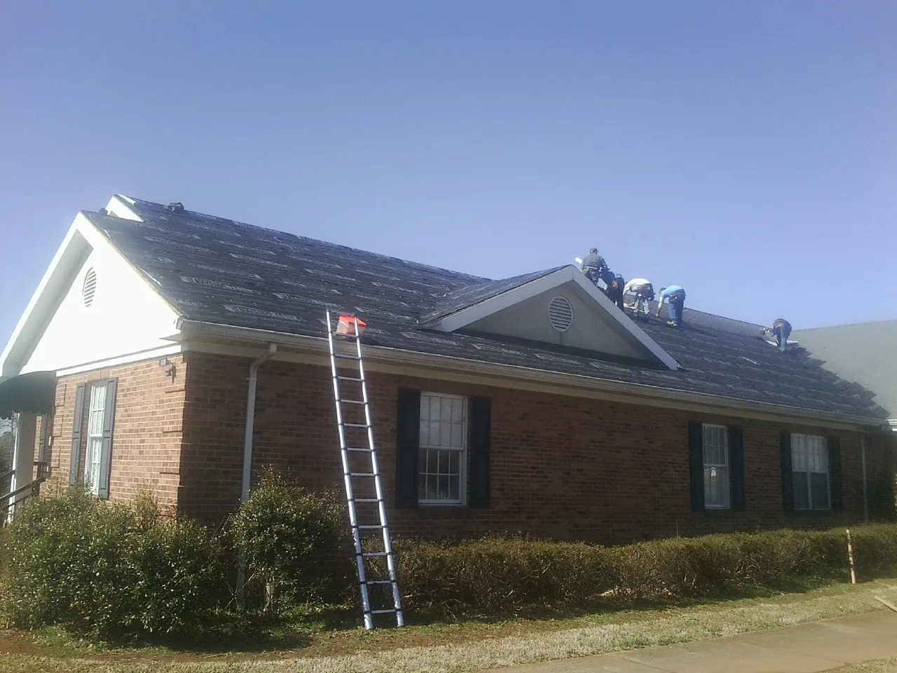 Crew tearing shingles off a brick ranch roof with a ladder set — Emergency Roof Repair work by our crew in El Sobrante
