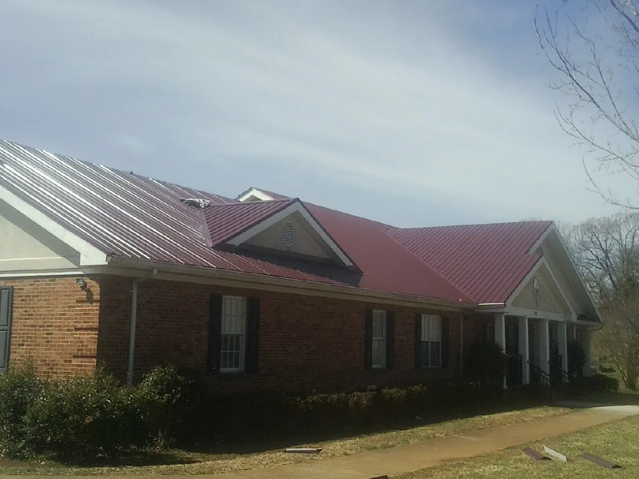 Red metal roof with gabled entries on a long brick building, from a Hail Damage Roof Repair job in El Sobrante