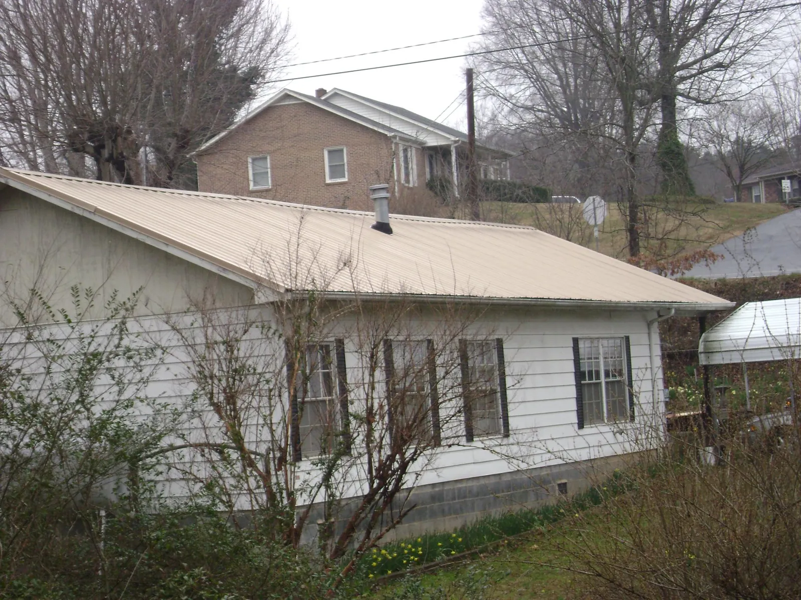 Tan metal roof on a white sided house set into a hillside — Commercial Roofing by Roofing Brothers in El Sobrante
